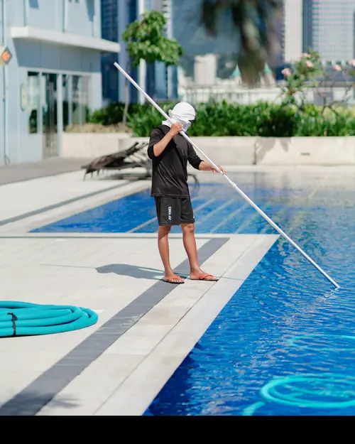 A pool technician cleaning the surface of a large blue pool with a pole