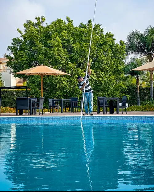 A pool technician skimming a clear blue pool with a long pole