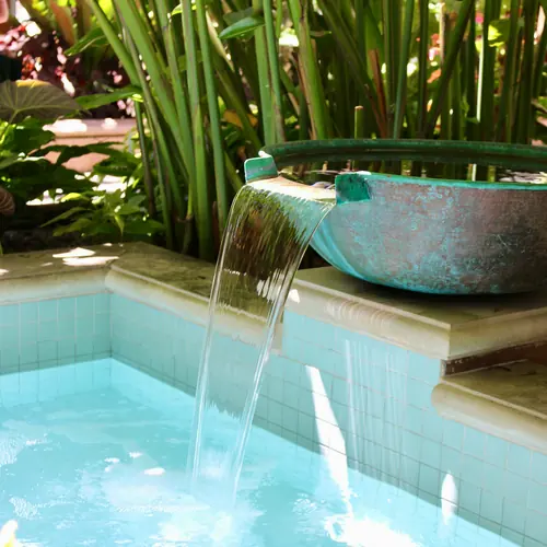 Clear water spilling from a copper bowl into a tiled aqua pool